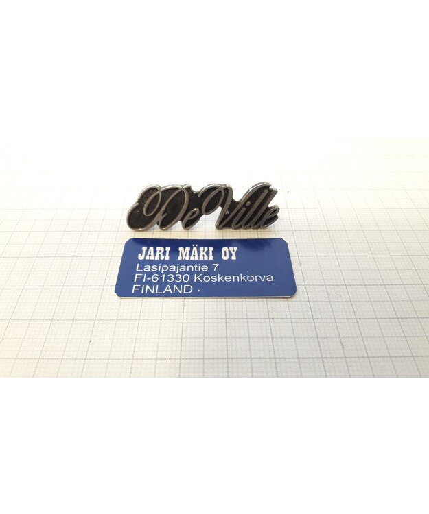 Merkki metallia "De Ville" kojetauluun Cadillac 1977-1984